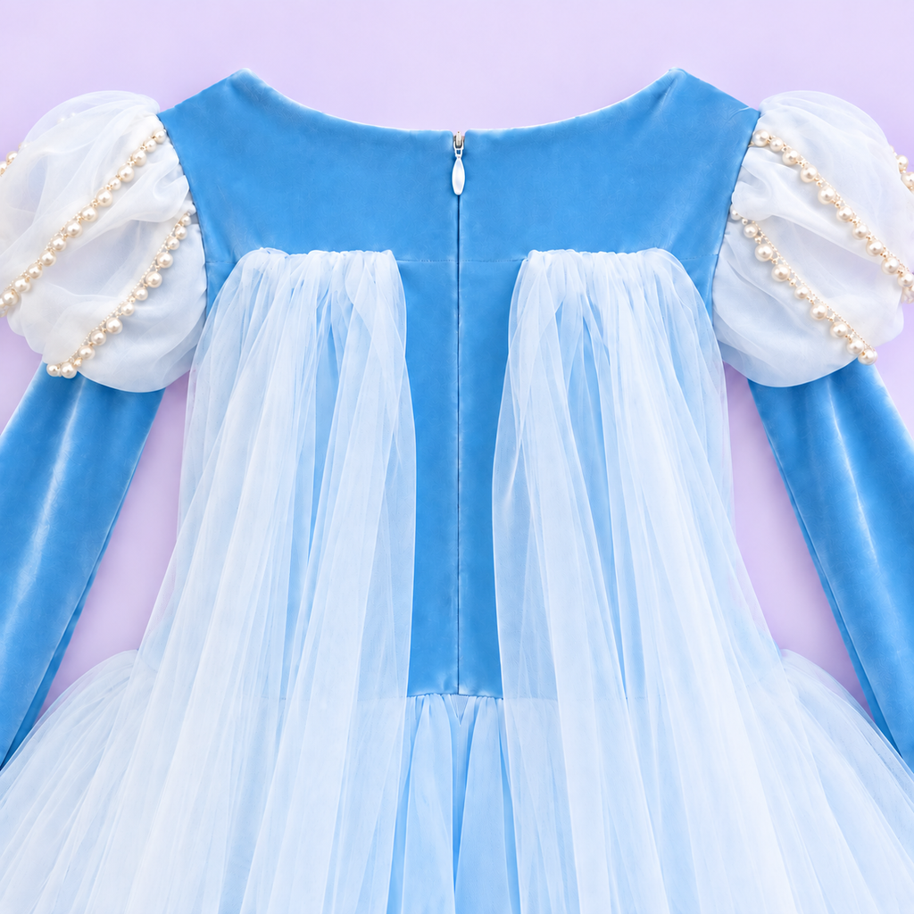  Elsa-inspired sky-blue princess dress in a white studio. The Frozen-inspired costume has a snowflake-embroidered bodice, pearl-trimmed white puff sleeves, long blue sleeves and a full skirt of fine white net over blue fabric. Her lower legs show faintly through the sheer hem.