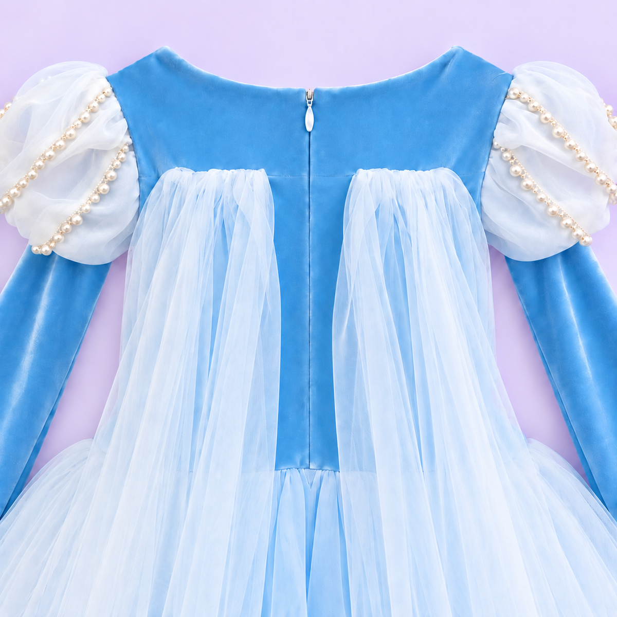  Elsa-inspired sky-blue princess dress in a white studio. The Frozen-inspired costume has a snowflake-embroidered bodice, pearl-trimmed white puff sleeves, long blue sleeves and a full skirt of fine white net over blue fabric. Her lower legs show faintly through the sheer hem.