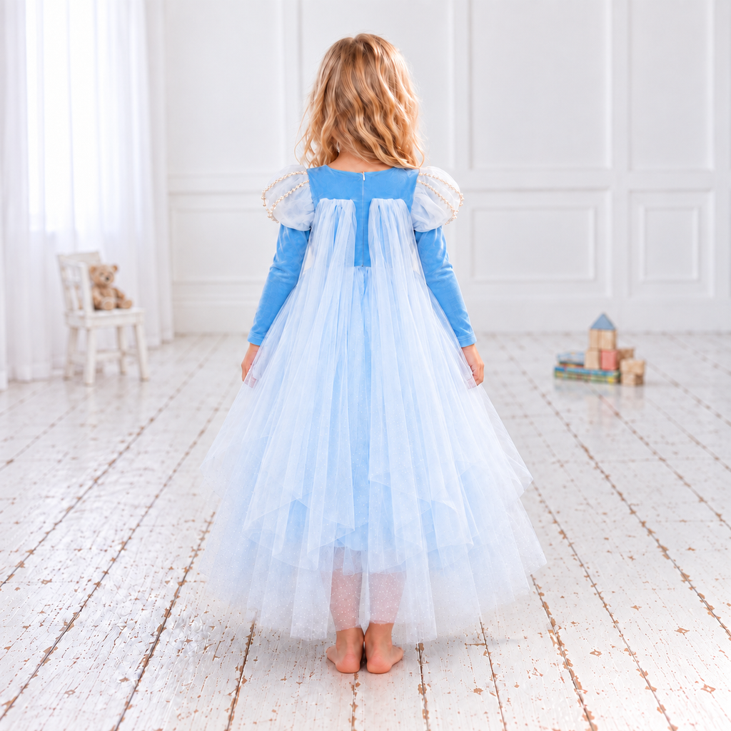  Elsa-inspired sky-blue princess dress in a white studio. The Frozen-inspired costume has a snowflake-embroidered bodice, pearl-trimmed white puff sleeves, long blue sleeves and a full skirt of fine white net over blue fabric. Her lower legs show faintly through the sheer hem.
