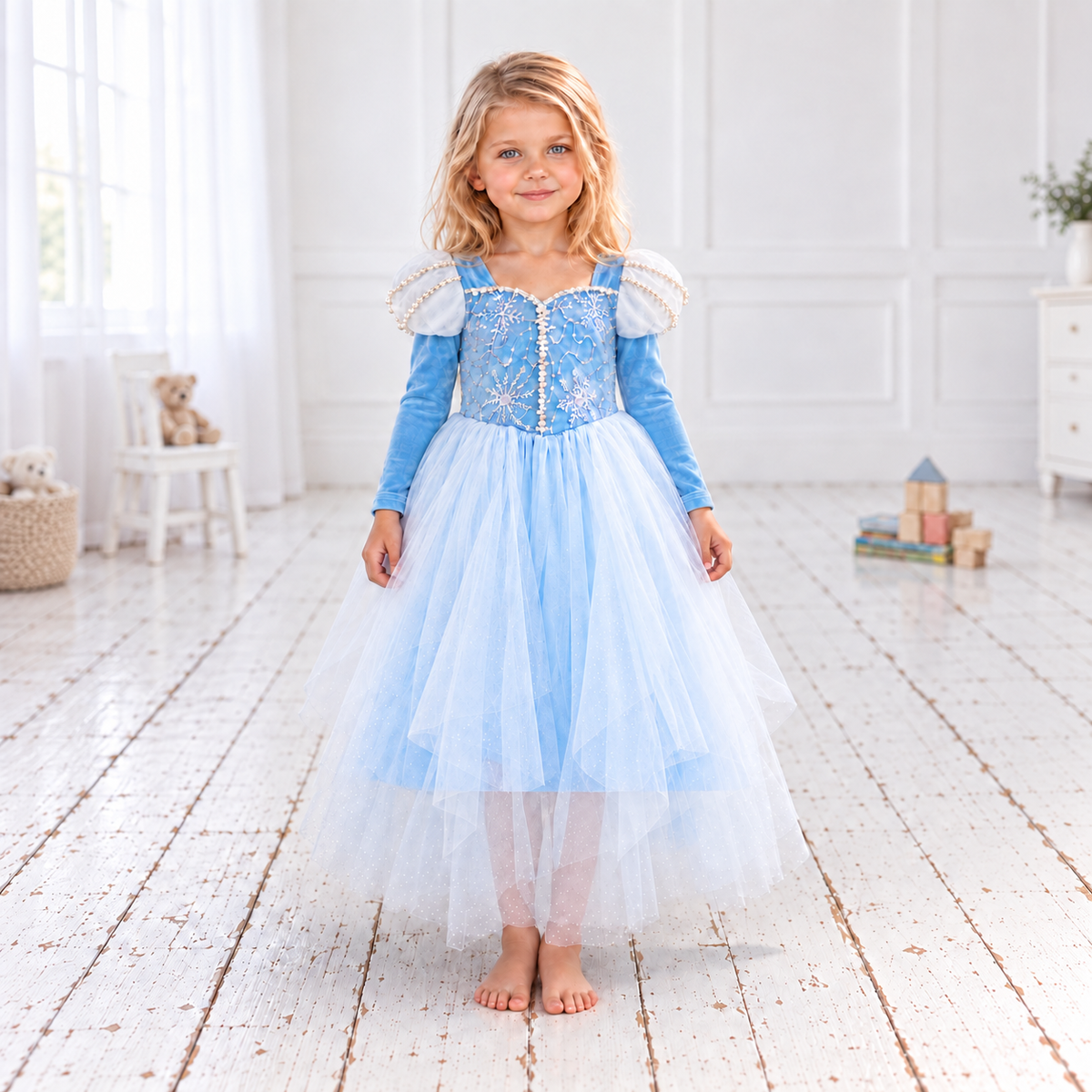  Elsa-inspired sky-blue princess dress in a white studio. The Frozen-inspired costume has a snowflake-embroidered bodice, pearl-trimmed white puff sleeves, long blue sleeves and a full skirt of fine white net over blue fabric. Her lower legs show faintly through the sheer hem.