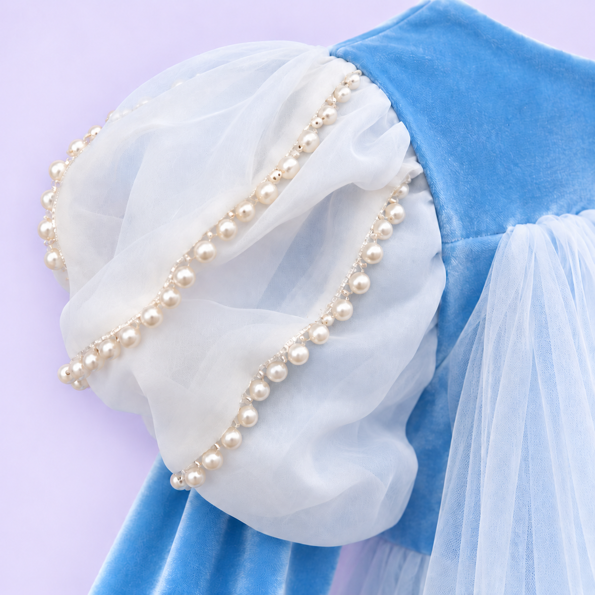  Elsa-inspired sky-blue princess dress in a white studio. The Frozen-inspired costume has a snowflake-embroidered bodice, pearl-trimmed white puff sleeves, long blue sleeves and a full skirt of fine white net over blue fabric. Her lower legs show faintly through the sheer hem.